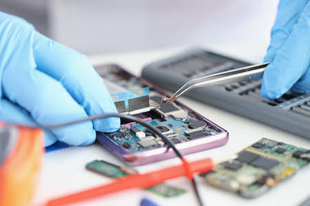 Hands in gloves hold a smartphone microchip with tweezersの写真素材