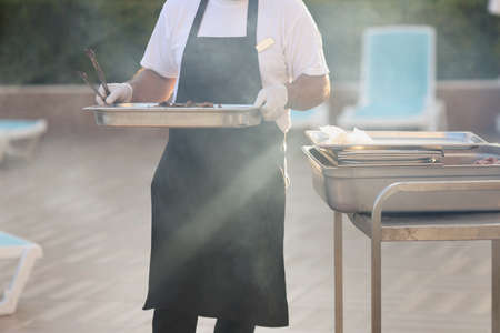 Chef carry cooked meal, metal construction for frying food, do grill, picnic outdoorsの写真素材