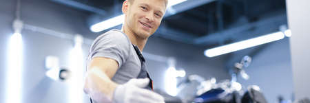 Smiling young car mechanic stands in workshop closeup