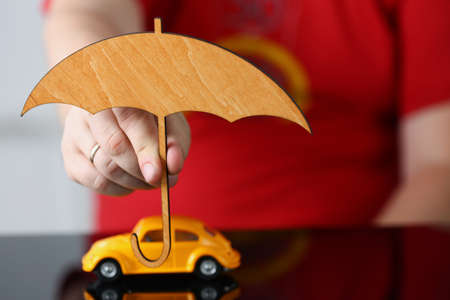 Woman hand holding wooden umbrella over car, symbol for car protectionの写真素材