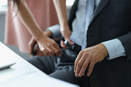 Secretary unzip boss belt at working place, harassment or work affairの写真素材