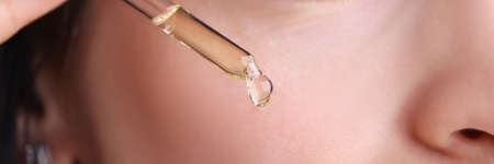 Woman holding dropper with cosmetic oil near her face closeup