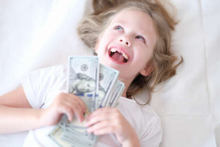 Little girl without front teeth holding money in her hands and smilingの写真素材