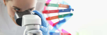 Woman scientist looking through microscope near dna molecule mockup in labの写真素材