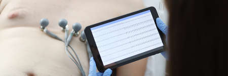 Doctor taking cardiogram to sick patient man on digital tablet in clinic closeupの写真素材