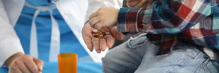 Little boy and doctor folding medical capsules in jar closeup