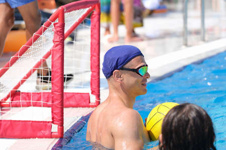 Man at gate in pool plays water polo.