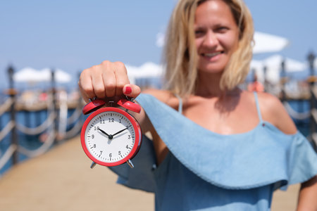 Smiling female tourist holding an alarm clock on sea pierの写真素材