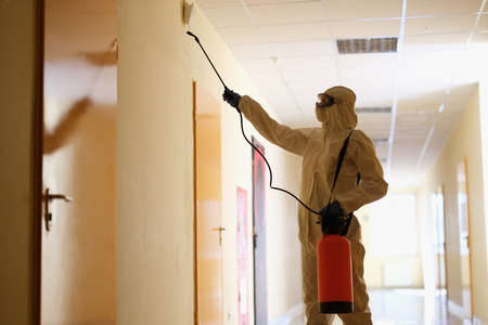 Specialist in protective suit disinfects premises in corridorの写真素材