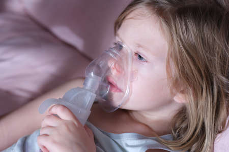 Sick little child in medical oxygen mask lying in bedの写真素材