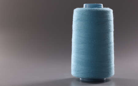 Blue colour thread spool on grey background, thread for dressmaking industry, yarn for sewing