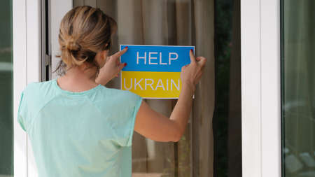 Woman sticking sign on door help Ukraine closeup