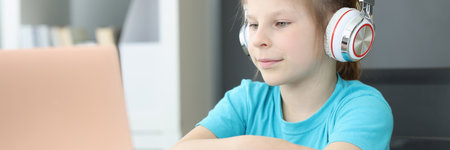 A student girl in headphones sits in front of a laptop