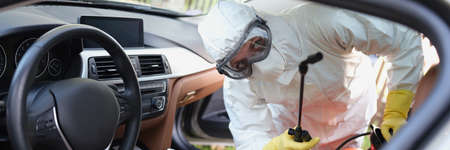 Person in protective costume clean surfaces in car with disinfectant sprayの写真素材