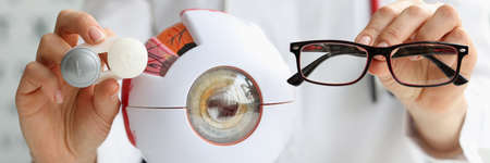 Ophthalmologist doctor holding eyeglasses and lenses near artificial model of eye closeupの写真素材
