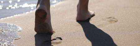 Barefoot female feet walking along sea beach closeupの写真素材