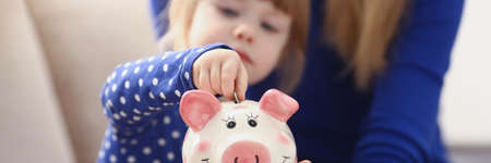 A little girl puts a coin in a pink piggy bankの写真素材