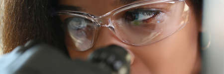A dark-skinned woman looks through a microscope