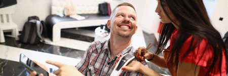 Female hairdresser and male client discuss future haircut in luxury beauty salon