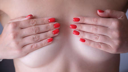 Woman with red manicure covering breasts with hands closeupの写真素材
