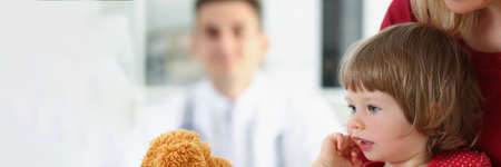 Little girl with mother play with teddy bear before doctor appointment