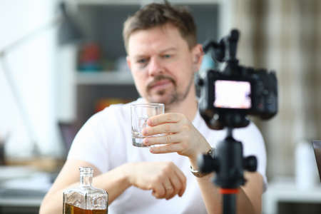 Exhausted man with black eye drinks alcohol in front of cameraの写真素材