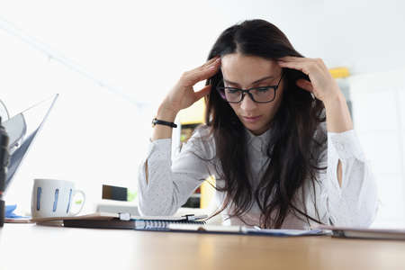 Tired sleepy woman sits at table holds head and rests at the workplace