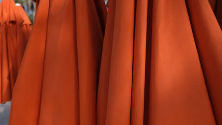 Red orange umbrellas stand stacked on beach