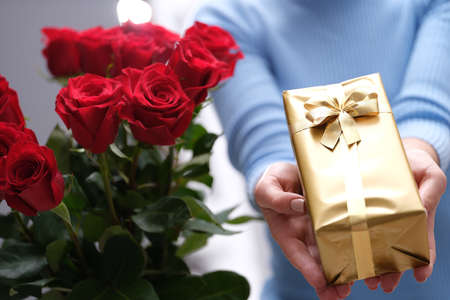 Bouquet of red roses and golden gift box in hands of courierの写真素材