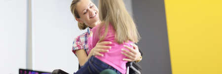Young woman sitting in wheelchair and hugging her little daughter