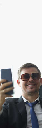 Businessman in sunglasses in suit looking at screen of mobile phoneの写真素材