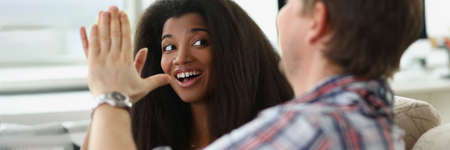 Caucasian man and african american woman sitting on sofa and giving high fiveの写真素材