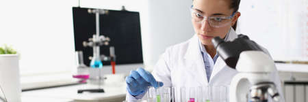 Chemist woman holding test tube with liquid in front of microscope in laboratory