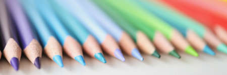 Many sharp multicolored pencils lying over colors of rainbow closeup backgroundの写真素材