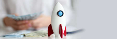 Toy rocket standing on table in front of woman with money closeupの写真素材