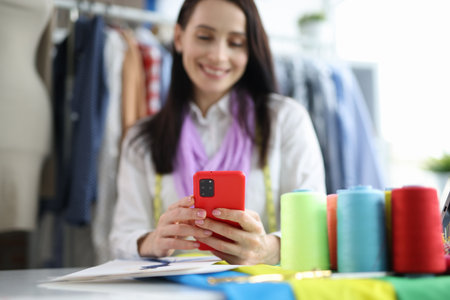 Beautiful fashion designer is sitting at table and typing on smartphone