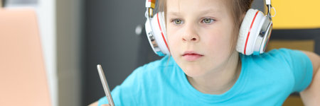 Little girl schoolgirl in headphones sitting in front of laptop at homeの写真素材