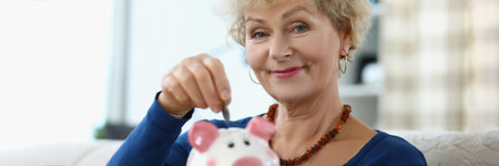 An elderly woman puts a coin in a piggy bankの写真素材
