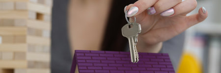 Female worker hand hold key to unlock new miniature toy house, buy new accommodationの写真素材