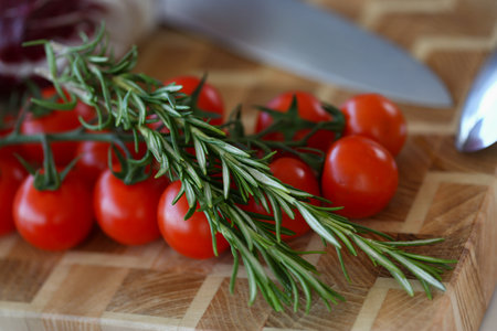 Organic cherry tomatoes with rosemary on wooden board with knifeの写真素材