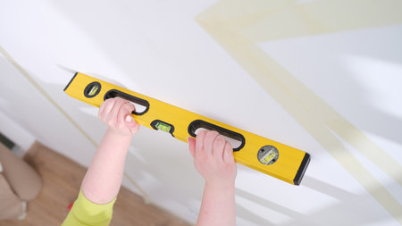 Hands of worker hold yellow level against white wall