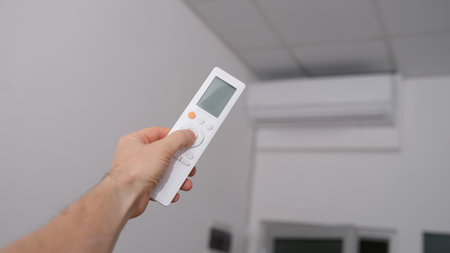 Hand with the remote control is directed to air conditionerの写真素材