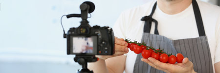Vlogger chef showing ripe tomatoes ingredient, man in apron recording red vegetableの写真素材