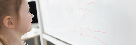 Toddler writing solution of sums on white board at school, educational process