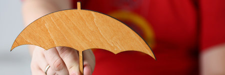 Woman hand holding wooden umbrella over car, symbol for car protectionの写真素材