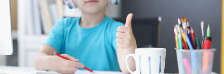 Schoolgirl studying online at home, wear headset, show thumbs up, drawing