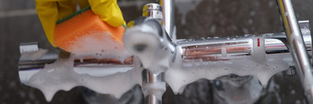 Cleaning lady in rubber glove washes faucet in bathroom with sponge with foamの写真素材