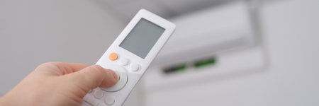 Hand with remote control is directed to air conditioner on wallの写真素材