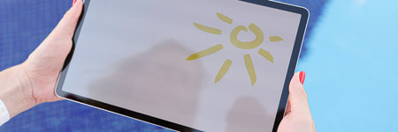 Female hands hold tablet with drawn sun and white screen above pool