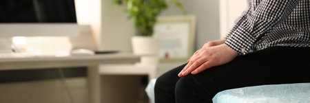 Closeup of young woman sitting on couch with folded hands on kneesの写真素材